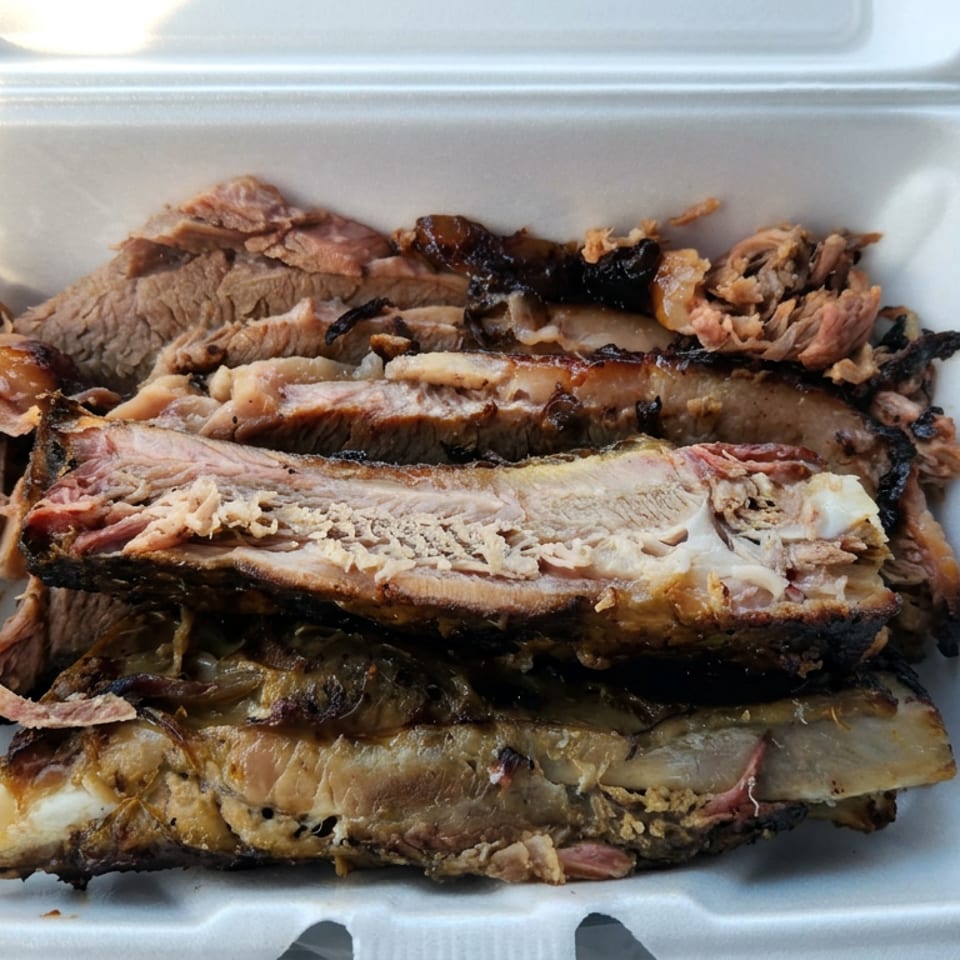 Stack of sliced grilled meat with charred edges served in an open white takeout container.