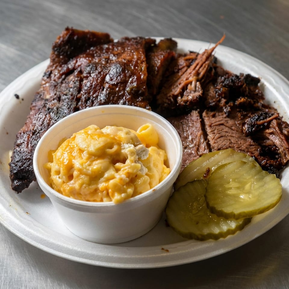 Barbecue platter with smoked ribs, sliced brisket, macaroni and cheese, and dill pickles on a white plate.