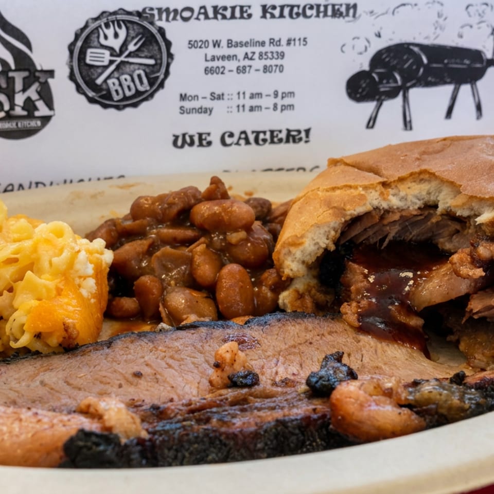 Barbecue platter featuring sliced smoked meat, a sauced pulled-pork sandwich, baked beans, and macaroni and cheese at Smokie Kitchen.